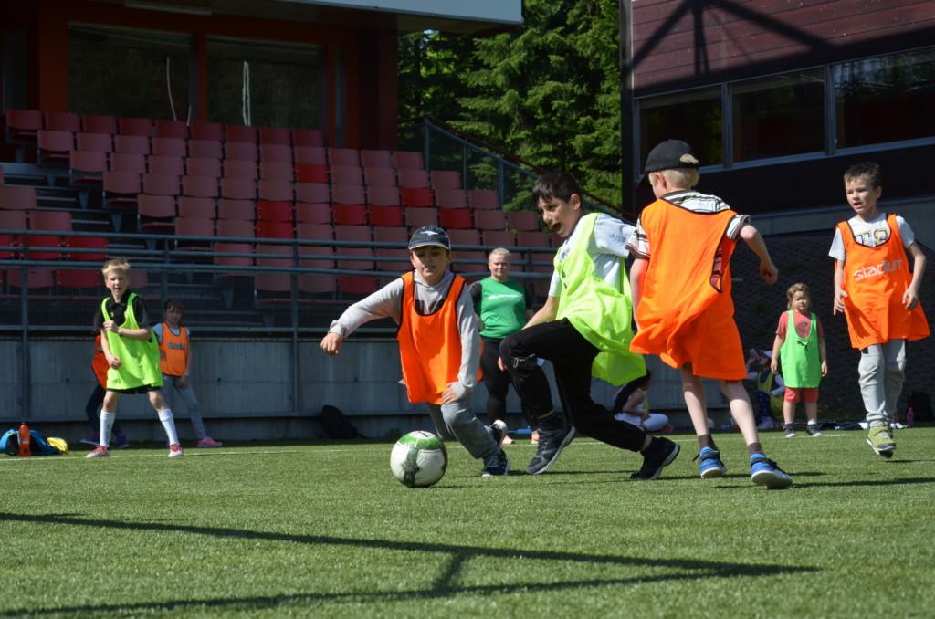 Oranssiliiviset ja keltaliiviset lapset pelaavat jalkapalloa tekonurmella.