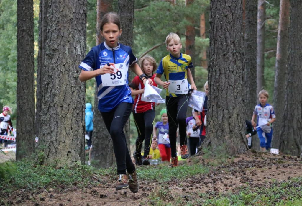 Suunnistusmaastossa lapsia puiden välissä juoksemassa